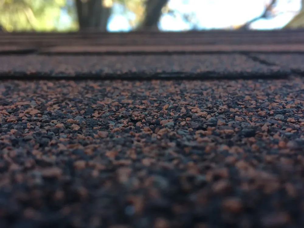 Close-up of asphalt shingle granules worn thin on an aging roof, with bare mat starting to show through