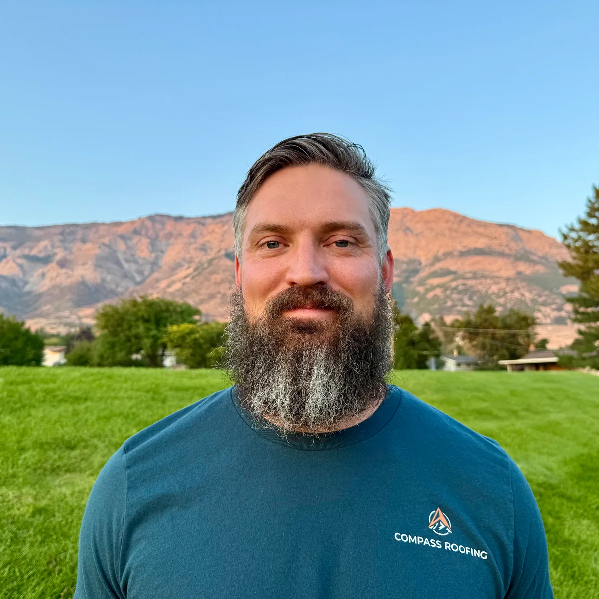 Cameron Husom, owner of Compass Roofing, in a Compass shirt with the Wasatch mountains behind him at sunset
