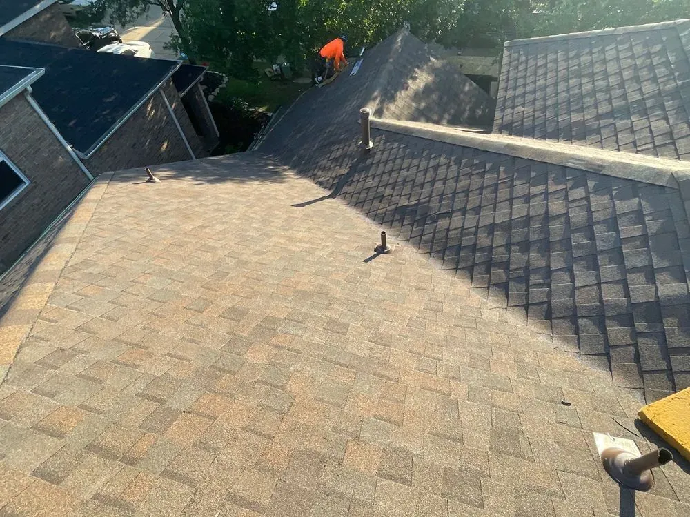 A roofing crew finishing a full asphalt shingle roof replacement, with new architectural shingles across multiple roof planes