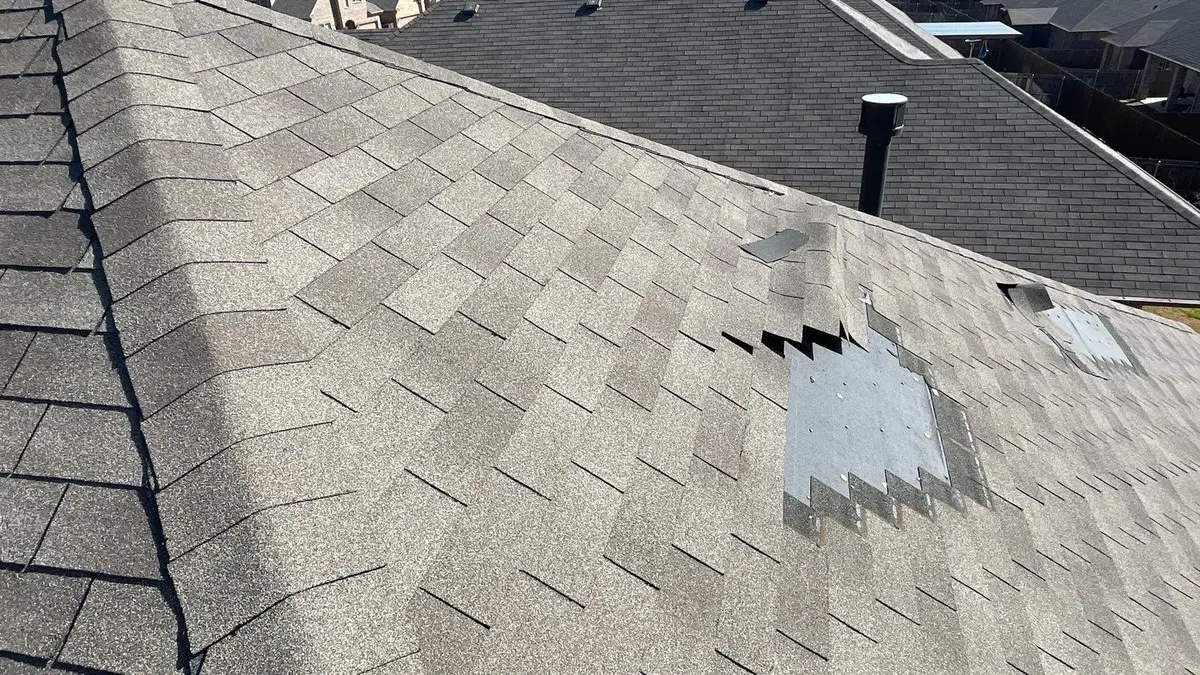 Wind-lifted, torn, and missing asphalt shingles on a residential roof, with underlayment exposed